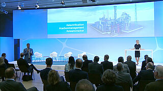 Ein Mann im Anzug vor beleuchteter Bühne spricht zu einem Publikum