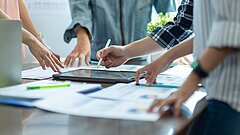 Besprechung mit mehreren Personen an Tisch mit Unterlagen