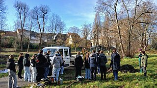 Schulklasse steht bei Pflanzarbeiten auf einer Wiese neben einem weißen Transporter