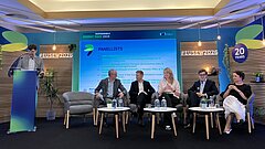 Panel discussion at EUSEW 2026: five people are seated side by side on the right; on the left, a man is standing at a lectern