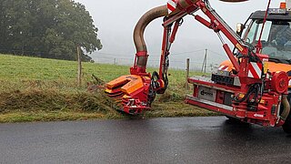 ein orangener Mähwagen fährt einer Wiese entlang und mäht den Rand