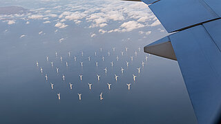 Eine Flugzeugtragfläche im Flug über einer Windkraftanlage im Meer.
