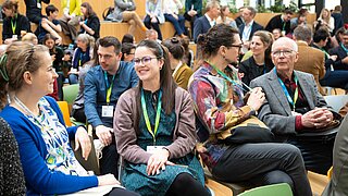 Viele Personen sitzen auf Stühlen und sprechen miteinander. 