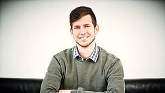 Projektkoordinator Matthias Dziubany sitzt hinter einem Tisch, die Arme verschränkt auf dem Tisch, , dahinter weißer Hintergrund