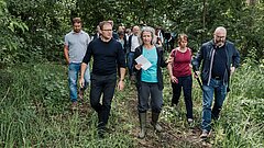 Umweltminister Carsten Schneider, Anje Marten (LfU) und Medienverterter*innen laufe über eine Wiese.