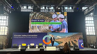 Ein Mann steht auf einer Bühne, im Hintergrund sieht man mehrere Bildschirme