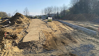 Baustelle mit aufgeschüttetem Erdreich, Reifenabdrücken im Boden und Randstein
