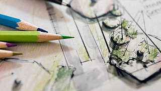 Buntstifte liegen auf einem Blatt Papier mit Skizzen