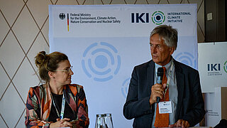 Dr. Kathrin Blaufuss und Andreas Kübler vom Bundesumweltministerium stehen an einem Rednertisch.stehen 