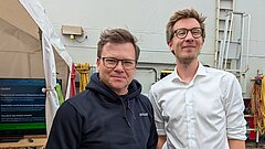 Zwei Männer (BU Carsten Schneider und Florian Börgel) blicken lächelnd in die Kamera