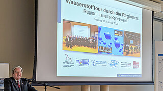 Wirtschaftsminister Steinbach steht vor einem Rednerpult, im Hintergrund läuft eine Präsentation