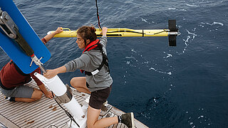 Two people on a ship retrieve a yellow sonar device from the seawater.