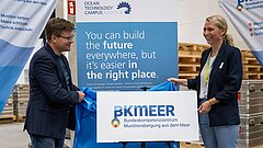 ein Mann (Carsten Schneider) und eine Frau (Julia Oldenburg) enthüllen ein Logo auf einem Gestell 