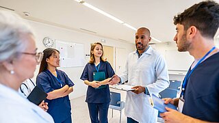 Mehrere Personen in medizinischer Kleidung stehen in einem Raum und sprechen miteinander