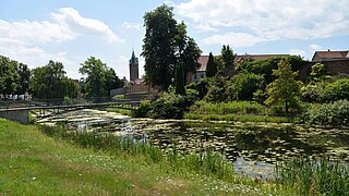 Blick auf einen Graben, im Hintergrund eine Stadt und einige Bäume