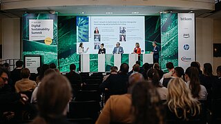 Meherere Personen stehen auf einer Bühne vor einem Publikum, im Hintergrund eine große Leinwand