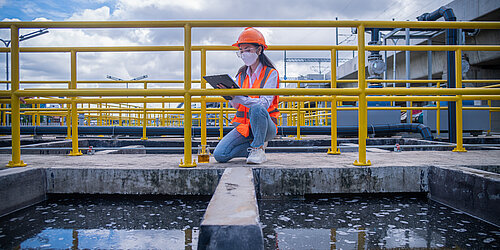 Frau in Schutzkleidung nimmt Probe aus Klärwerk