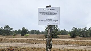 Ein Schild mit Hinweis auf ein Naturschutzgebiet, im Hintergrund Bäume