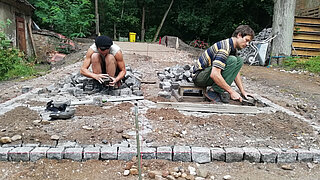 Zwei Männer knien auf dem Boden und verlegen Pflastersteine
