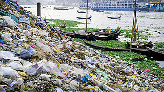 Piles of plastic waste on a river bank with boats