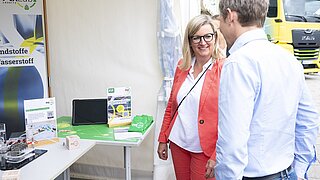 Brandenburgs Wirtschaftsministerin Martina Klement steht am Stand des PtX Lab Lausitz beim Brandenburger Energietag und spricht mit einem Vertreter des PtX Lab Lausitz.