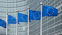Mehrere Flaggen der Europäischen Union wehen vor der Glasfassade eines modernen Bürogebäudes.