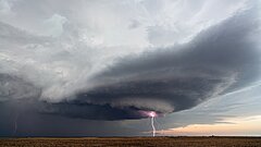 Das Bild zeigt eine große Gewitterwolke über einem Feld, auf das ein Blitz einschlägt