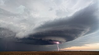Das Bild zeigt eine große Gewitterwolke über einem Feld, auf das ein Blitz einschlägt