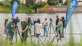 People stand in front of a river with cameras