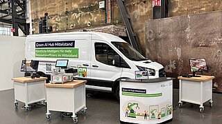 Ein Lieferwagen steht in einer Messehalle, davor befinden sich Messestand und einige Rollcontainer mit Geräten