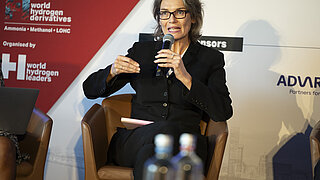 PtX-Referentin Anja Paumen als Panelistin auf einem Podium während der World Hydrogen Derivatives Conference in Rotterdam. In ihrer Hand hält sie ein Mikrofon.