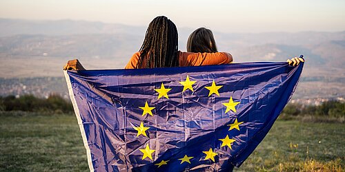 Zwei Jugendliche vor einem Bergpanorama halten eine Europa-Flagge