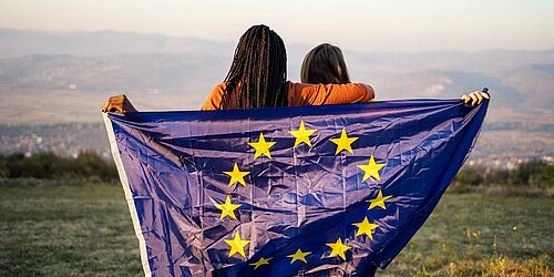 Zwei Jugendliche vor einem Bergpanorama halten eine Europa-Flagge