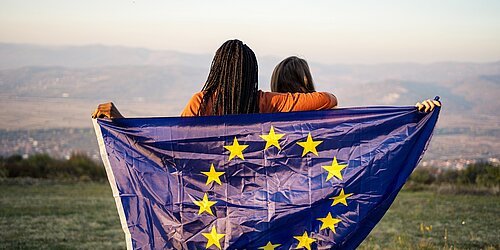 Two young people in front of a mountain panorama hold an EU flag
