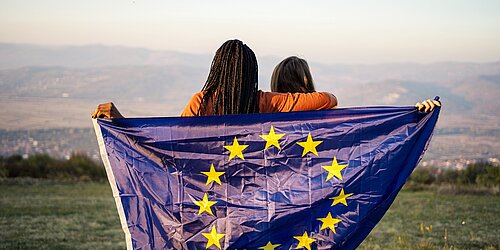 Zwei Jugendliche vor einem Bergpanorama halten eine Europa-Flagge