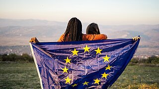 Two young people in front of a mountain panorama hold an EU flag