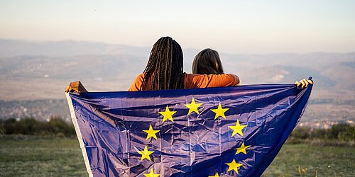 Zwei Jugendliche vor einem Bergpanorama halten eine EU-Flagge