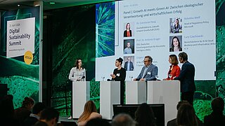 Eine Bühne mit Bildschirm und mehreren Sprechern/Sprecherinnen